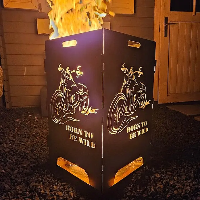 TiKo-Design Holzkohlegrill Feuerkorb-Born to be wild - Grau - Dunkle Metall-Feuerstelle mit Motorrad-Designs und 'Born to be Wild'-Text, im Freien mit Feuer leuchtend.