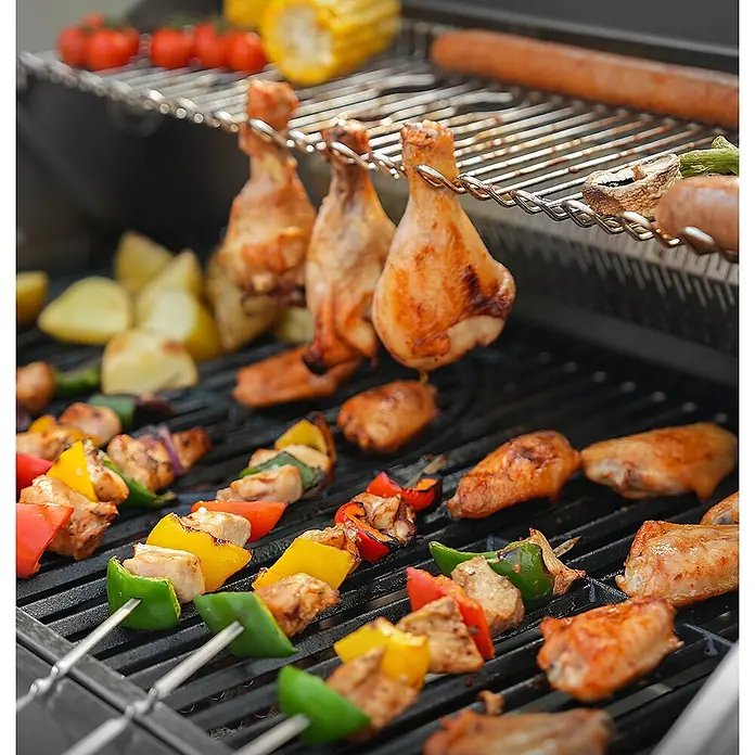 TAINO Gasgrill PLATINUM YAMARA 4+2 - Anzahl Brenner: 4 Stk. - Dunkler Metallgrill mit grillenden Hähnchenschenkeln, Spießen, Würstchen, Gemüse und Mais.