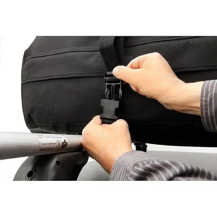 Fischer Caja de techo - L x An x Al: 100 x 80 x 40 cm, Metal, Capacidad volumétrica: 270 l, Peso de carga máx.: 50 kg - Manos abrochando una bolsa de techo de coche de tela negra a una barra de techo plateada.