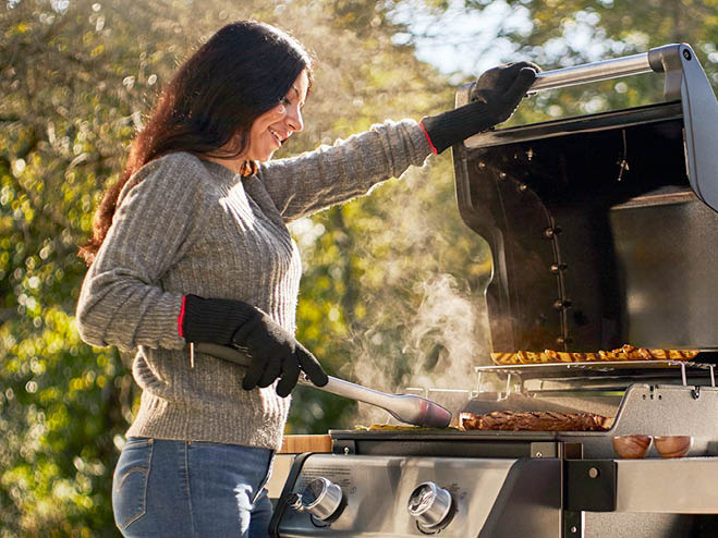 Frau steht am Balkon beim WEBER Grill und grillt Gemüse und Fleisch