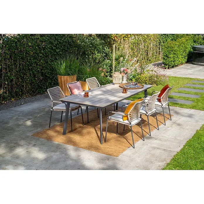 Garden Impressions Gartensessel Swifty - 1 Stk., Stahl, Polyester, Stapelbar, Beige, B x T x H: 63,5 x 84,5 x 56,5 cm - Eine Outdoor-Essgruppe mit hellem Holztisch und sechs Stühlen mit geflochtenen Rückenlehnen und Kissen auf einem Terrassenteppich.