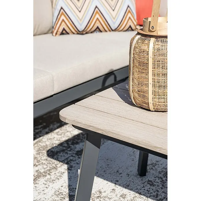 Garden Impressions Loungemöbel-Set Terni - 3 -tlg., Aluminium, Grau/Schwarz - Nahaufnahme eines hellen Outdoor-Kaffeetisches mit Holzoptik und grauen Beinen, daneben eine Korblaterne und ein Sofa.