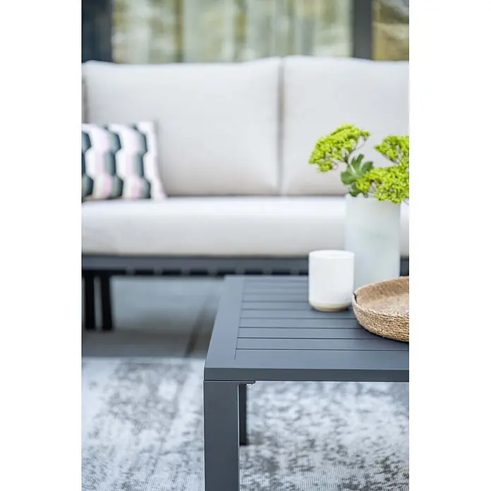 Garden Impressions Loungemöbel-Set - 4 -tlg., Aluminium, Ecklounge, Grau/Schwarz - Dunkelgrauer Latten-Gartentisch mit weißem Kerzenhalter, geflochtenem Korb und Vase, Teil einer Loungemöbel-Garnitur im Freien.