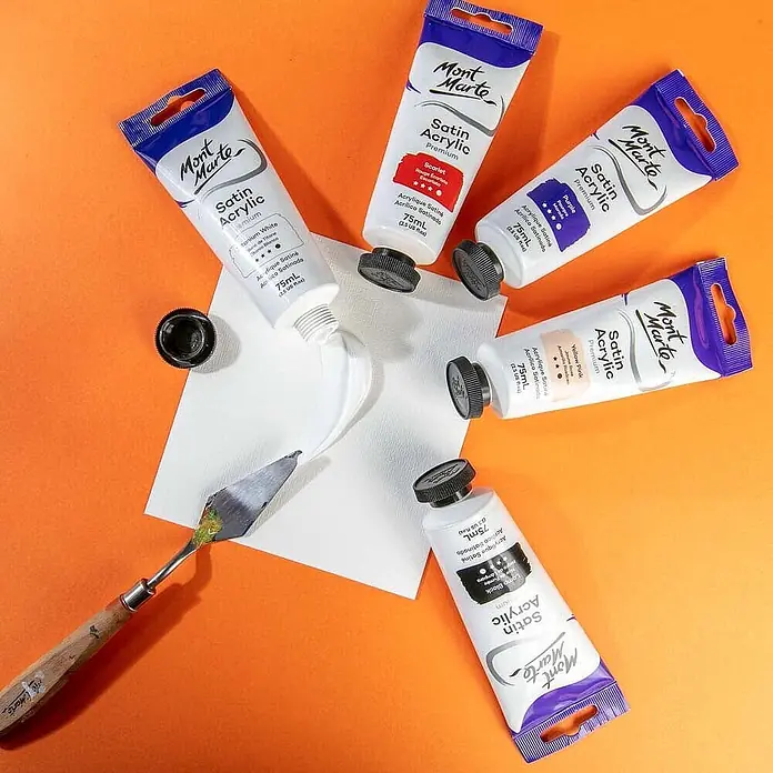 Mont Marte Acrylfarbe Premium - Titanweiß, 75 ml, Tube - Mont Marte Satin Acrylfarbtuben in verschiedenen Farben mit einem Spachtel, eine Tube gibt weiße Farbe auf Papier ab.