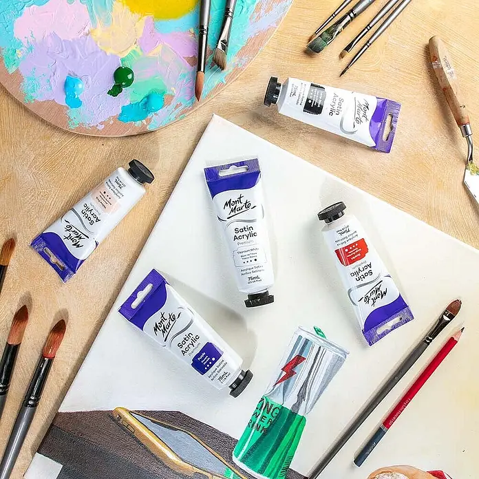 Mont Marte Acrylfarbe Premium - Titanweiß, 75 ml, Tube - Mont Marte Satin Acrylfarben in Tuben, Pinsel, eine Palette mit gemischten Farben und ein unfertiges Energy-Drink-Gemälde auf einer Leinwand.