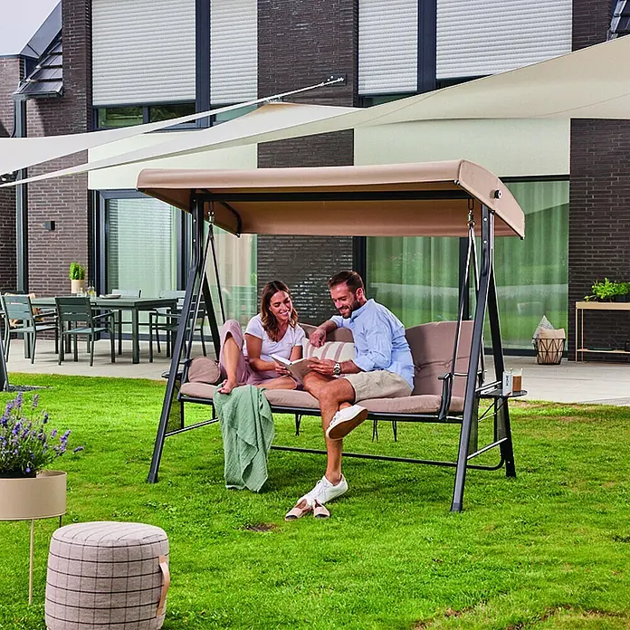 Home Deluxe Garten-Schaukelstuhl Hollywoodschaukel DESCANSO - Beige, B x T x H: 115 x 198 x 195 cm - Eine braune Gartenschaukel mit dunklem Metallrahmen, die von einem Paar genutzt wird.