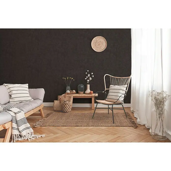 A.S. Création New Walls Vliestapete I - Schwarz, Uni, 10,05 x 0,53 m - Einladendes Wohnzimmer mit minimalistischem Holzstuhl, bequemen Kissen und einem rustikalen Teppich auf hellem Holzboden.