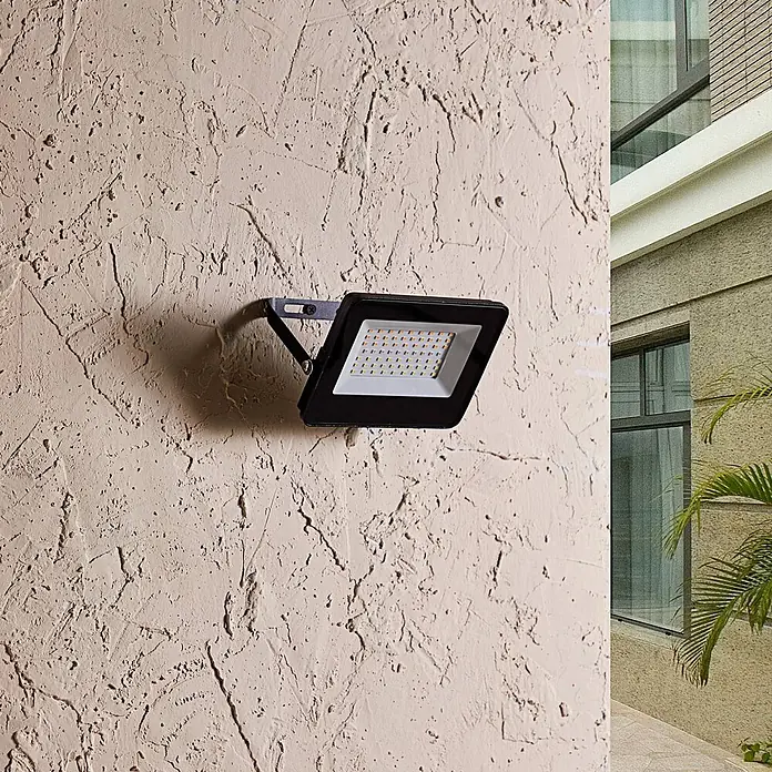 Prios LED-Strahler Liezel - L x B x H: 17 x 13 x 14 cm - Schwarzer LED-Flutlichtstrahler an einer strukturierten Außenwand montiert.