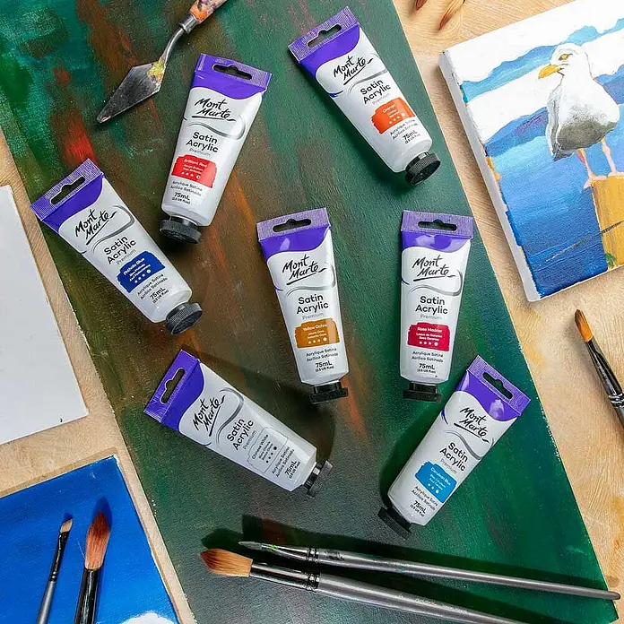 Mont Marte Acrylfarbe Premium - Ocker Gelb, 75 ml, Tube - Auswahl an Mont Marte Satin Acrylfarben-Tuben in verschiedenen Farben, mit Malwerkzeugen und Kunstwerken arrangiert.