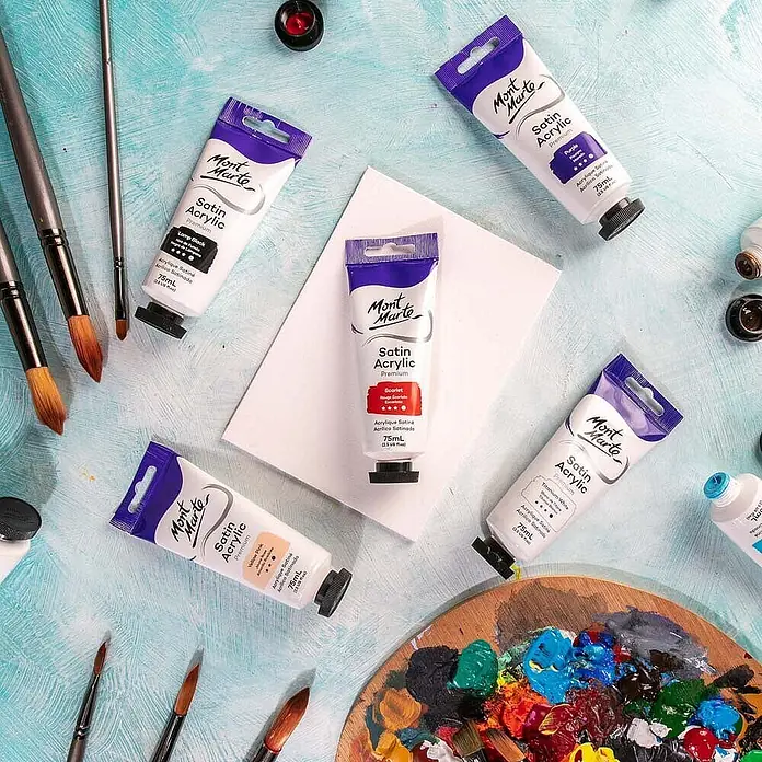 Mont Marte Acrylfarbe Premium - Scharlachrot, 75 ml, Tube - Eine Auswahl Mont Marte Satin Acrylfarben, Pinsel und eine Palette mit Farbmischungen auf blauem Untergrund.