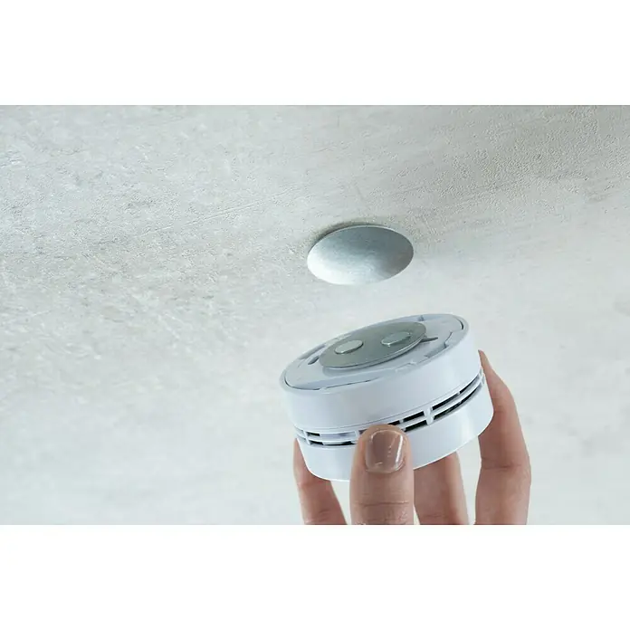 Mini-Rauchmelder-Befestigung - Durchmesser: 4 cm, Kleben - Eine Hand hält einen weißen Rauchmelder, der an der Decke montiert werden soll. Ein Sicherheitsgerät für das Haus.