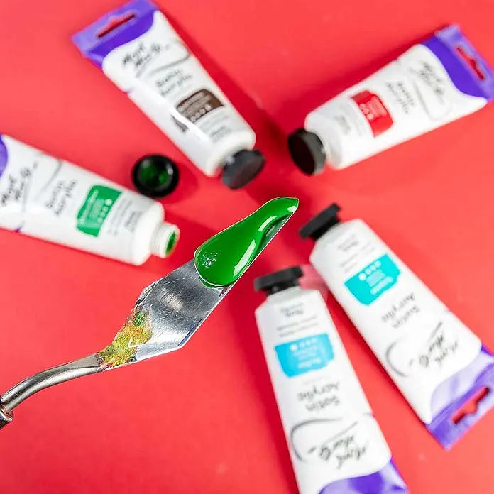 Mont Marte Acrylfarbe Premium - Mittelgrün, 75 ml, Tube - Grüne Acrylfarbe auf einem Spachtel, mit verschiedenen Farbtuben auf roter Oberfläche.