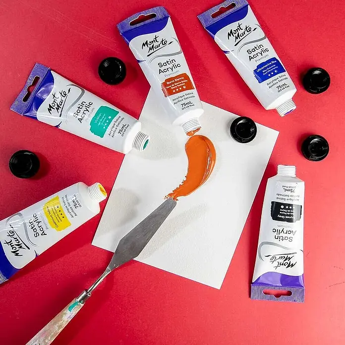 Mont Marte Acrylfarbe Premium - Gebrannte Siena, 75 ml, Tube - Mehrere Mont Marte Satin Acrylfarben-Tuben mit orangefarbener Farbe auf weißem Papier neben einem Spachtel.