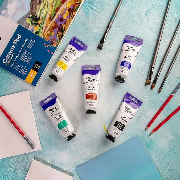 Mont Marte Acrylfarbe Premium - Gebrannte Siena, 75 ml, Tube - Mont Marte Satin Acrylfarben, Pinsel, Leinwandblöcke und Bleistifte auf einer strukturierten blaugrünen Oberfläche.