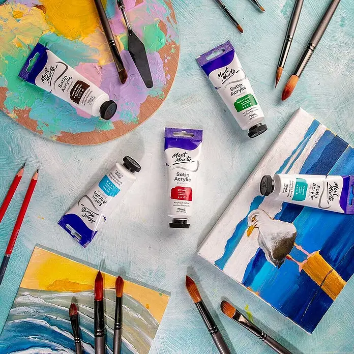 Mont Marte Acrylfarbe Premium - Karminrot, 75 ml, Tube - Mont Marte Satin Acrylfarben-Tuben in verschiedenen Farben, umgeben von Künstlerbedarf wie Pinseln und Leinwänden.