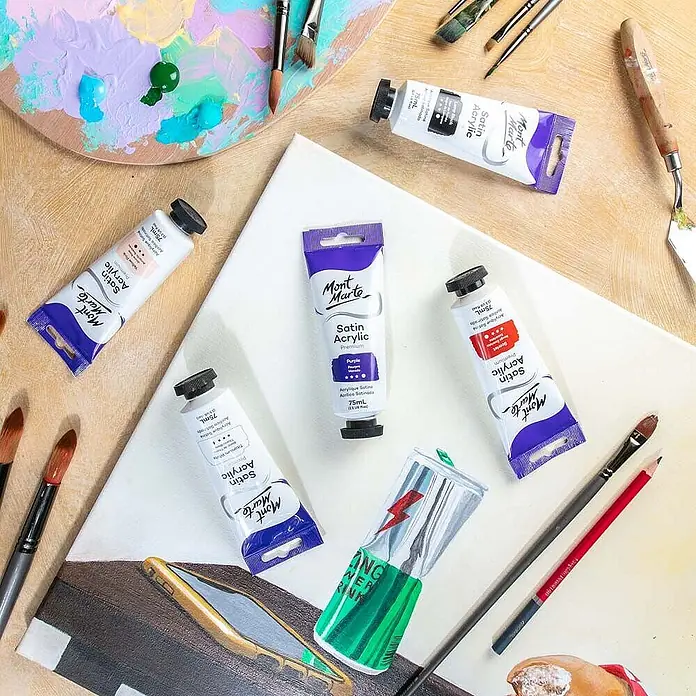 Mont Marte Acrylfarbe Premium - Violett, 75 ml, Tube - Mont Marte Satin Acrylfarben-Tuben, Pinsel und Palette auf einer Leinwand, die eine Malsitzung zeigen.