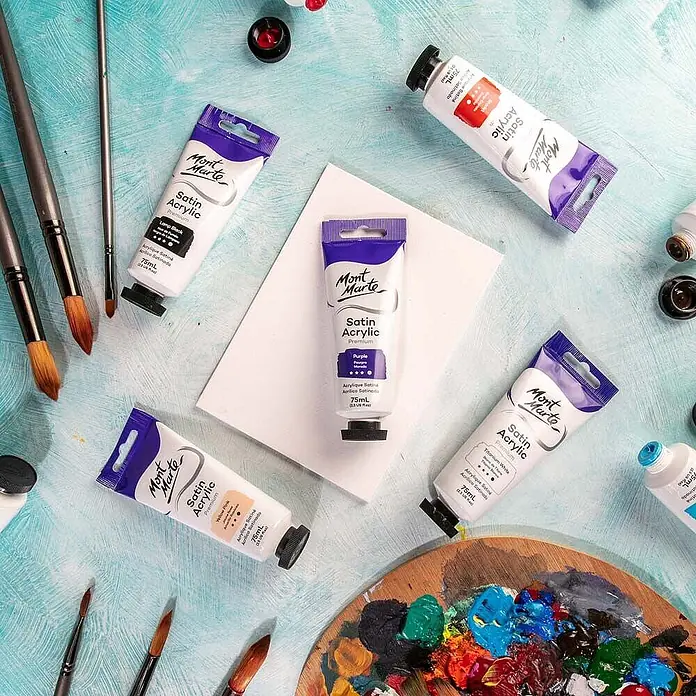 Mont Marte Acrylfarbe Premium - Violett, 75 ml, Tube - Mont Marte Satin Acrylfarben in verschiedenen Farben, Pinsel und eine Palette mit Farbmischungen auf blauem, texturiertem Untergrund, bereit zum Malen.