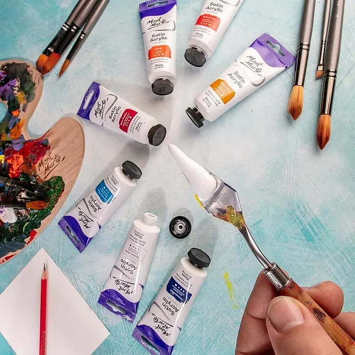 Mont Marte Acrylfarbe Premium - Chinesisch Weiß, 75 ml, Tube - Mont Marte Satin Acrylfarben in Tuben, Pinsel und eine Palette mit Farbe, von einer Hand mit Spachtel gehalten.