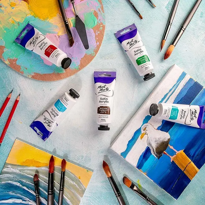 Mont Marte Acrylfarbe Premium - Gebrannte Umbra, 75 ml, Tube - Mont Marte Satin Acrylfarben, Pinsel und Künstlerbedarf auf hellblauem Untergrund mit kleinen Leinwänden und Palette.