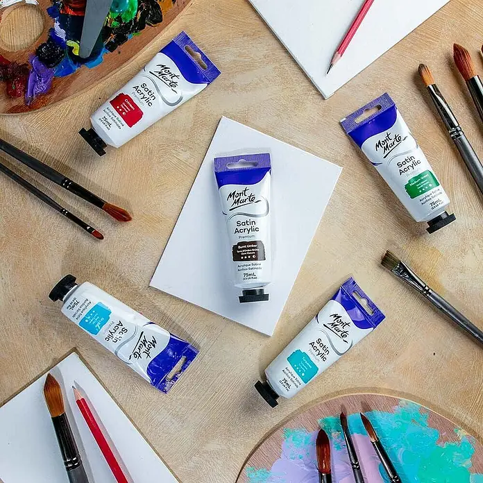 Mont Marte Acrylfarbe Premium - Gebrannte Umbra, 75 ml, Tube - Mont Marte Satin Acrylfarbtuben in verschiedenen Farben mit Pinseln, Palette und Leinwänden auf Holzoberfläche.