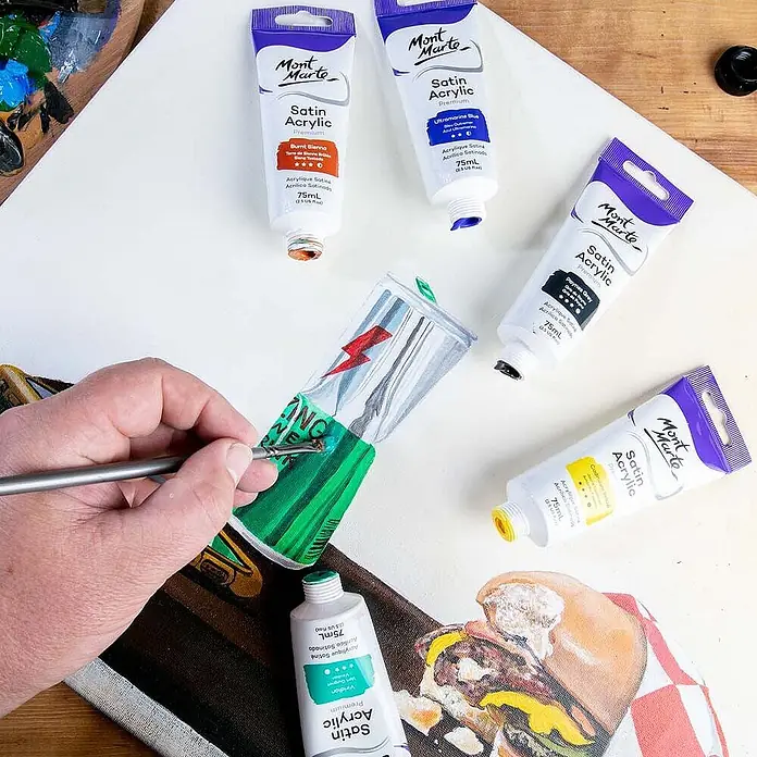 Mont Marte Acrylfarbe Premium - Viridiangrün, 75 ml, Tube - Eine Hand malt mit grüner Mont Marte Satin Acrylfarbe auf Leinwand, umgeben von anderen Farbtuben.