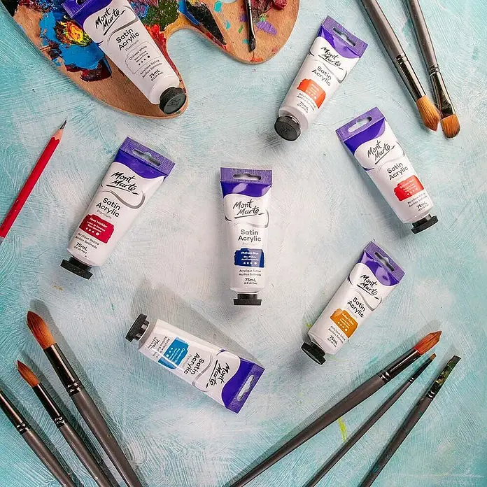 Mont Marte Acrylfarbe Premium - Phthaloblau, 75 ml, Tube - Mont Marte Satin Acrylfarben in Tuben verschiedener Farben und Pinsel auf einer strukturierten hellblauen Oberfläche mit Holzpalette.