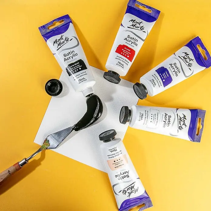 Mont Marte Acrylfarbe Premium - Lampenschwarz, 75 ml, Tube - Mont Marte Satin Acrylfarbtuben in mehreren Farben, mit schwarzer Farbe auf einer weißen Fläche neben einem Spachtel.