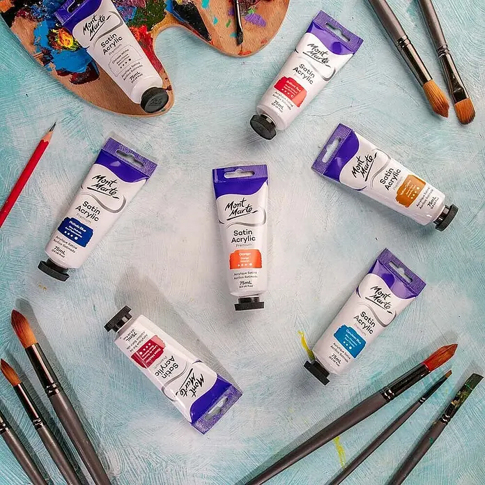 Mont Marte Acrylfarbe Premium - Orange, 75 ml, Tube - Mont Marte Satin Acrylfarben in Tuben, Pinsel und Palette auf einem strukturierten blauen Untergrund.