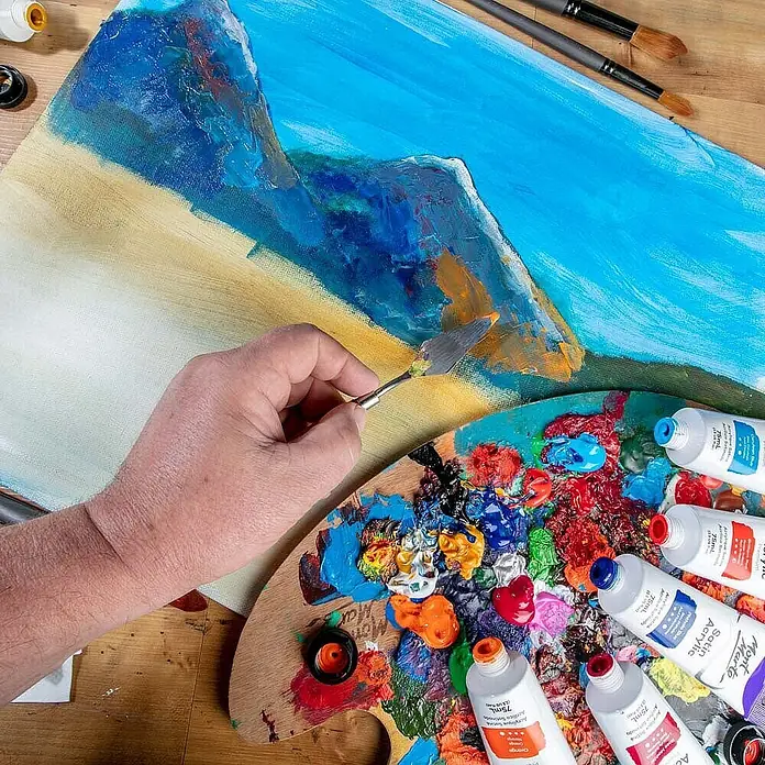 Mont Marte Acrylfarbe Premium - Orange, 75 ml, Tube - Hand malt abstraktes Landschaftsbild mit Spachtel auf Leinwand, umgeben von bunten Acrylfarben und Tuben.