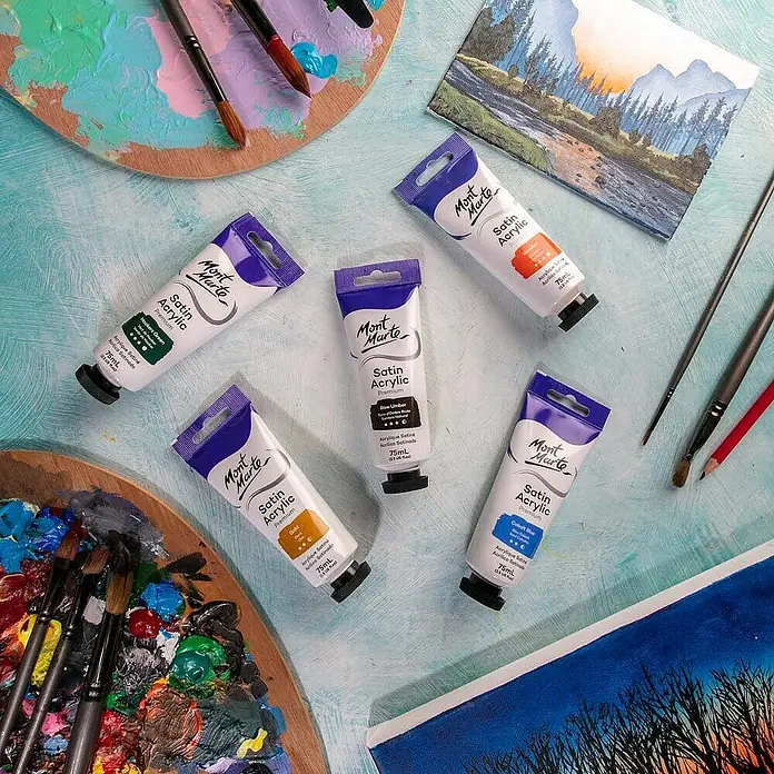 Mont Marte Acrylfarbe Premium - Natürliche Umbra, 75 ml, Tube - Mont Marte Satin Acrylfarben in verschiedenen Farben auf einem Künstlertisch mit Paletten, Pinseln und Gemälden.