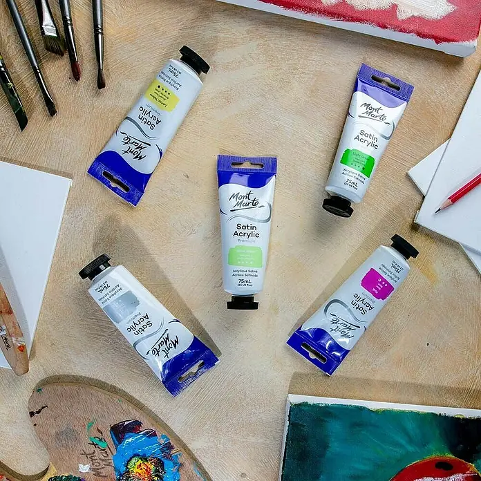 Mont Marte Acrylfarbe Premium - Gelbgrün, 75 ml, Tube - Eine Auswahl an Mont Marte Satin Acrylfarbtuben in verschiedenen Farben, zusammen mit Pinseln und Leinwänden auf einem Holztisch.