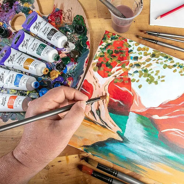 Mont Marte Acrylfarbe Premium - Gold, 75 ml, Tube - Eine Hand malt ein Kunstwerk auf Leinwand mit Mont Marte Acrylfarben, einer Holzpalette und verschiedenen Pinseln.