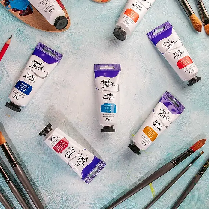 Mont Marte Acrylfarbe Premium - Zeruleanblau, 75 ml, Tube - Mehrere Mont Marte Satin Acrylfarben-Tuben, Pinsel und Palette auf hellblauem Untergrund für Kunstbedarf.