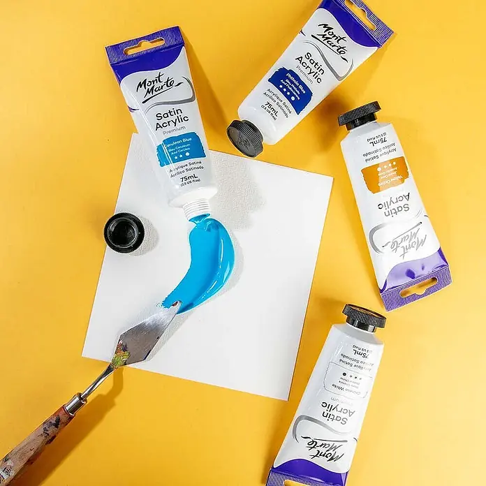 Mont Marte Acrylfarbe Premium - Zeruleanblau, 75 ml, Tube - Mont Marte Satin Acrylfarbtuben in Blau, Gelb und Weiß, mit blauer Farbe auf Papier gedrückt und mit einem Spachtel verteilt.