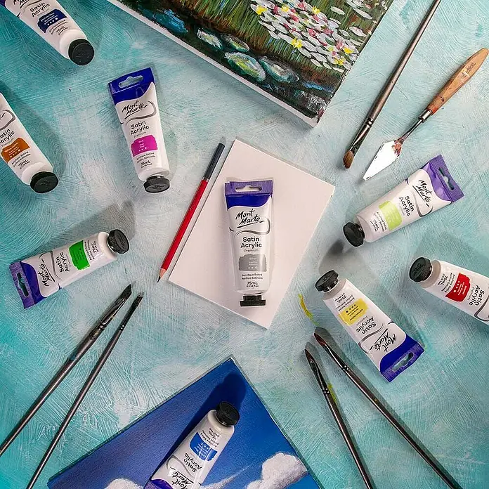 Mont Marte Acrylfarbe Premium - Silber, 75 ml, Tube - Sortiment Mont Marte Satin Acrylfarben in Tuben, umgeben von Pinseln und kleinen Leinwandgemälden.