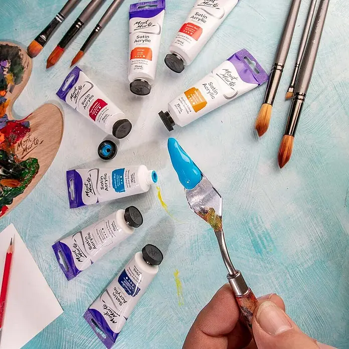 Mont Marte Acrylfarbe Premium - Zeruleanblau, 75 ml, Tube - Verschiedene Mont Marte Satin Acrylfarben-Tuben, Pinsel und ein Spachtel mit leuchtend blauer Farbe, bereit zum Malen.