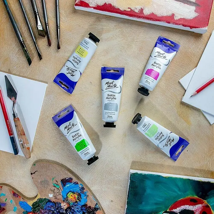 Mont Marte Acrylfarbe Premium - Silber, 75 ml, Tube - Mont Marte Satin Acrylfarben-Tuben und Künstlerbedarf wie Pinsel und Palette, zum Malen angeordnet.