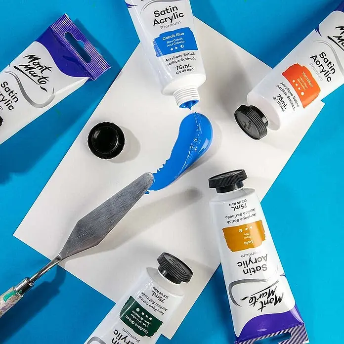 Mont Marte Acrylfarbe Premium - Kobaltblau, 75 ml, Tube - Auswahl an Mont Marte Satin Acrylfarben (Kobaltblau, Vermilion, Gold, Hooker's Green) mit blauer Farbe auf weißem Papier und Spachtel.