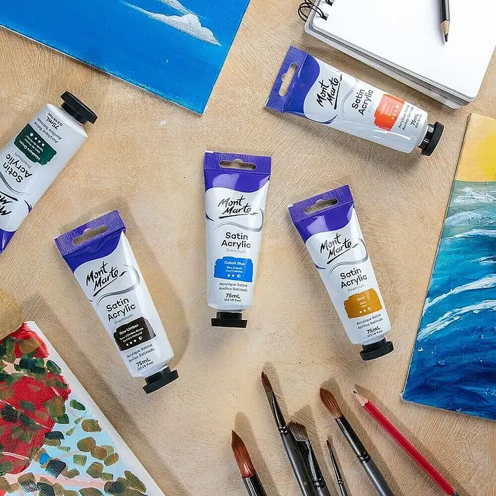 Mont Marte Acrylfarbe Premium - Kobaltblau, 75 ml, Tube - Mont Marte Satin Acrylic Farb-Tuben (grün, blau, gold, braun, orange) und Pinsel auf Holztisch mit Leinwänden, bereit zum Malen.