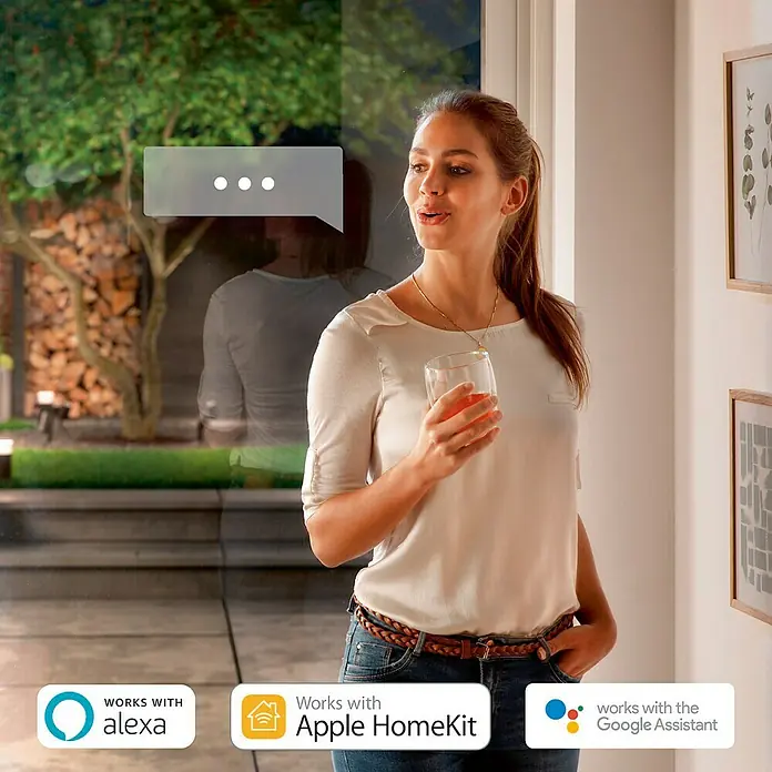 Philips Hue LED-Außenwandleuchte White & Color Ambiance Resonate Up & Down - 16 W, 9,3 x 12 x 18 cm, Schwarz, IP44 - Eine Frau, die ein Getränk hält, steht vor einem Fenster und interagiert mit Alexa, Apple HomeKit und Google Assistant.