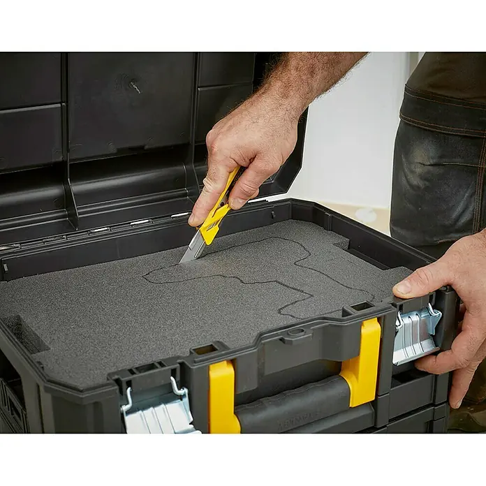 Stanley TSTAK Caja para herramientas FMST1-71967 - An x Pr x Al: 33,17 x 44 x 18,5 cm, Plástico - Hombre cortando un inserto de espuma en una caja de herramientas Stanley con un cúter amarillo.