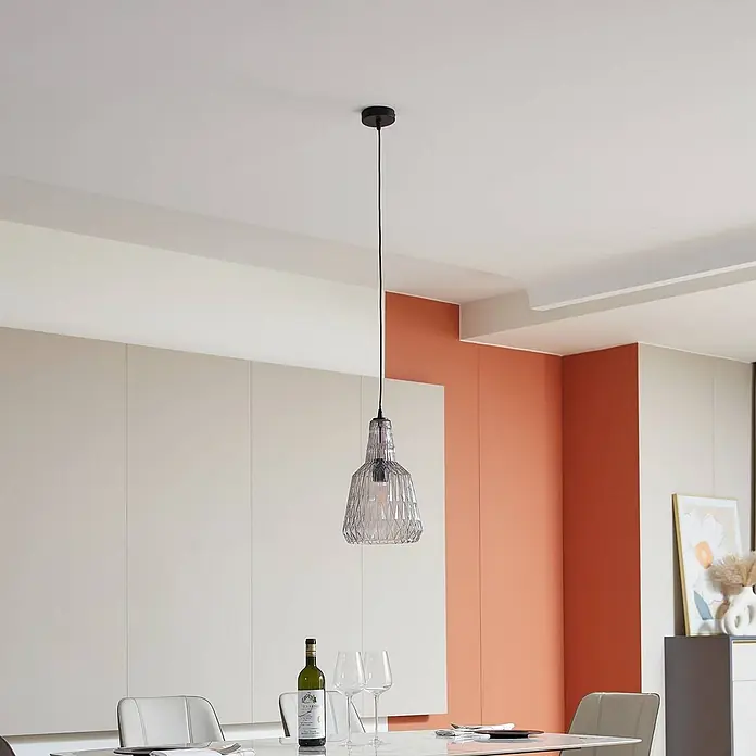 Lindby Pendelleuchte Belarion - L x B x H: 23 x 23 x 35 cm, alu / grau / zink, rauchgrau, E27 - Pendelleuchte aus klarem, gemustertem Glas mit schwarzem Kabel über einem Esstisch.