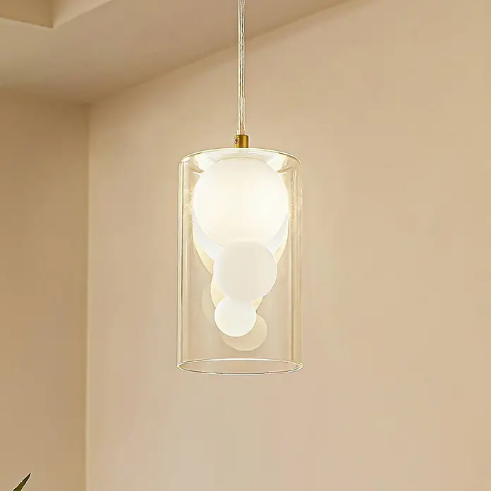 Lindby Pendelleuchte Kupla - L x B x H: 12 x 12 x 20 cm, klar / transparent, transparent, weiß, G9 - Eine moderne Pendelleuchte mit klarem zylindrischem Glasschirm und mehreren weißen Kugeldiffusoren im Inneren, hängt in einem Raum.