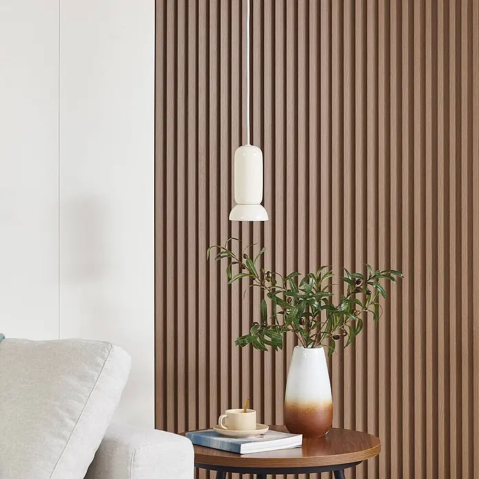 Lindby Pendelleuchte Kerimi - weiß / opal, creme, GU10 - Creme-zylindrische Pendelleuchte in modernem Interieur, beleuchtet eine strukturierte Holzwand und einen Beistelltisch.
