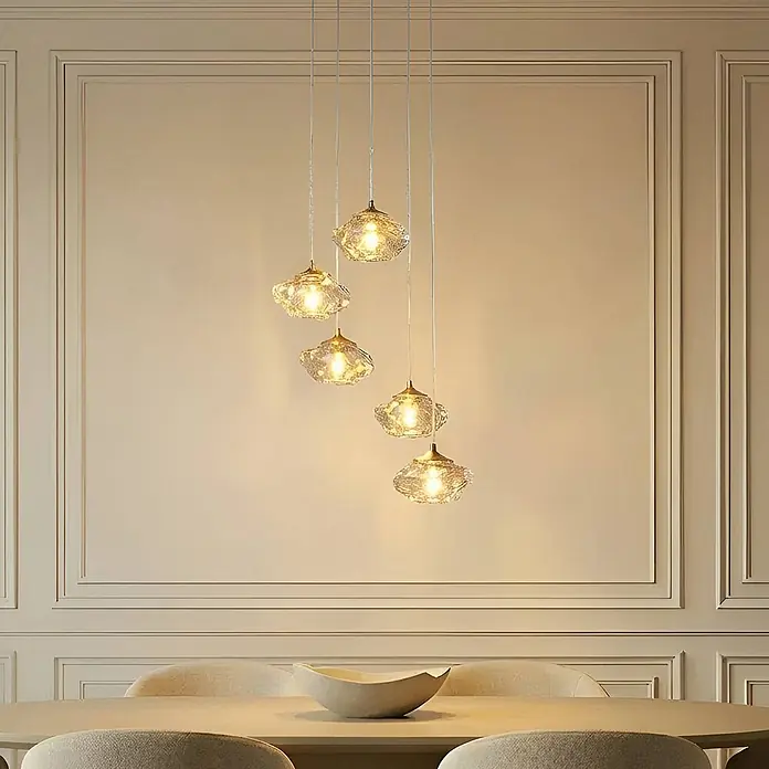 Lindby Pendelleuchte Piatra - L x B x H: 44,5 x 44,5 x 150 cm, creme / amber, amber, messing, G9 - Fünf Pendelleuchten aus strukturiertem Glas mit Goldakzenten hängen über einem Esstisch.