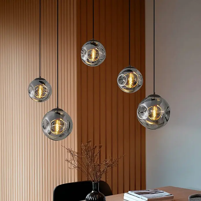 Lindby Pendelleuchte Valentina - alu / grau / zink, rauchgrau, kaffee, E27 - Fünf moderne Pendelleuchten aus Rauchglas mit Kugelformen und warmen Glühfadenbirnen, über einem Holztisch hängend.