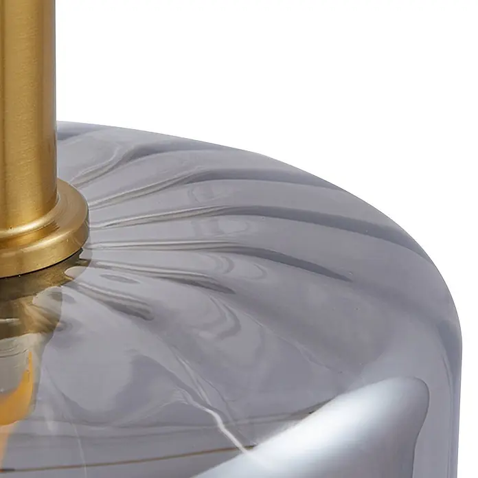 Lindby Pendelleuchte Hildur - alu / grau / zink, rauchgrau, messing, E27 - Nahaufnahme eines Lampenfußes mit goldfarbenem Metallschaft auf grauem, gemasertem Glas.