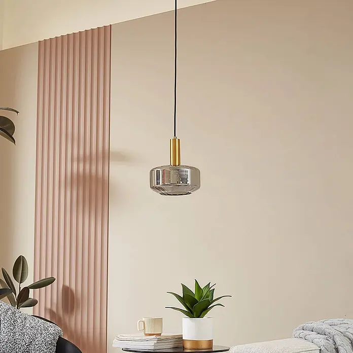 Lindby Pendelleuchte Hildur - alu / grau / zink, rauchgrau, messing, E27 - Moderne Pendelleuchte mit Rauchglasschirm und messingfarbenem Anschluss, an schwarzem Kabel im Raum hängend.