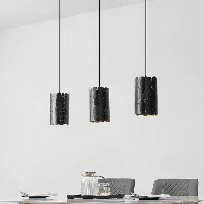Lindby Pendelleuchte Aralena - L x B x H: 92 x 15 x 25 cm, schwarz, Schwarz, gold, E27 - Drei schwarze zylindrische Pendelleuchten mit goldenen Mustern über einem Esstisch hängend.