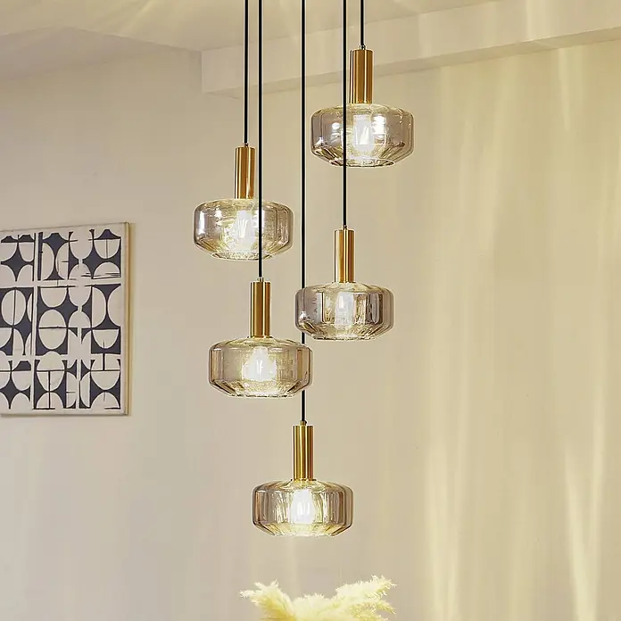 Lindby Pendelleuchte Hildur - L x B x H: 51,2 x 35 x 11,8 cm, alu / grau / zink, rauchgrau, messing, E27 - Fünf moderne Pendelleuchten mit Goldakzenten und geriffelten Glasschirmen hängen in einer Gruppe in einem Raum.